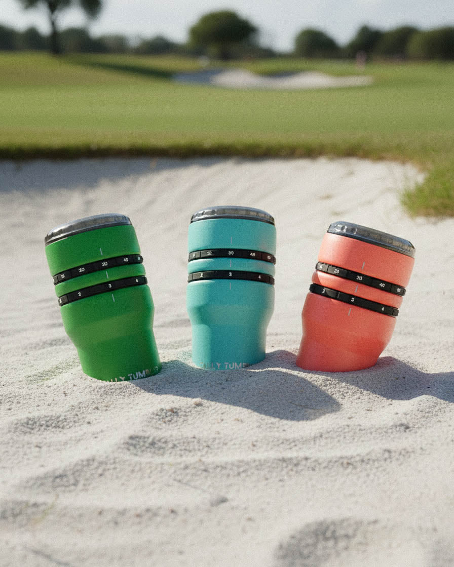 Three colorful tumblers on a sandy surface with a golf course background