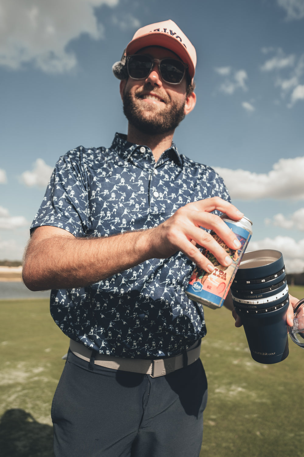 Man holding a drink and a can outdoors with a scenic background